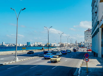 Cars on road by sea against sky in city