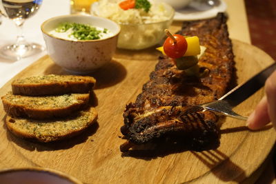 Cropped hands cutting meat with fork and knife on table