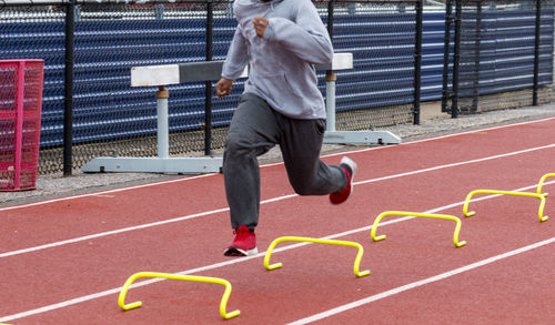 A track runner is running over small yellow hurdles performing the wicket  drill during practice.