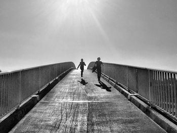 Low angle view of boys running on footbridge against sky during sunrise