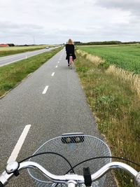Rear view of woman cycling on road against sky