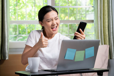 Young woman using phone while sitting on table