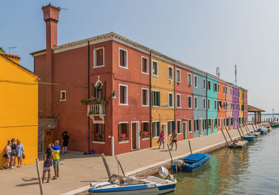 People on boats in canal by buildings against clear sky