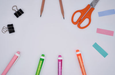 Directly above shot of multi colored pens with adhesive notes and scissors on gray background