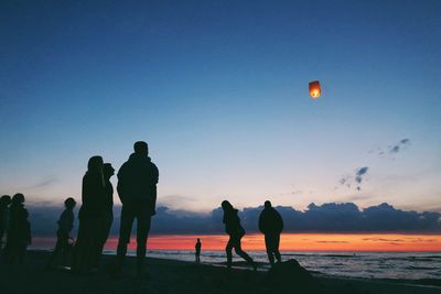 People at beach against sky at sunset