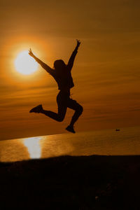 Silhouette man jumping on beach during sunset