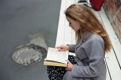 Side view of young woman reading book while sitting outdoors
