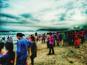 Group of people on beach against cloudy sky