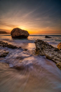 Scenic view of rocks in sea against sky during sunset