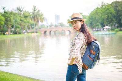 Side view portrait of woman with backpack standing by lake in park