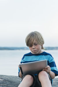 Boy using digital tablet at water