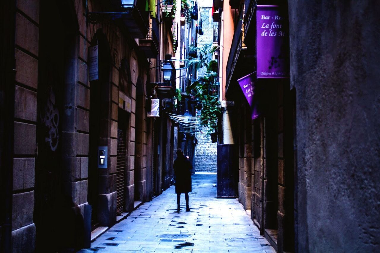 REAR VIEW OF WOMAN WALKING ON ALLEY AMIDST BUILDINGS