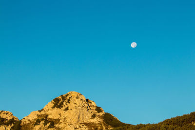 Low angle view of moon in mountain against clear blue sky