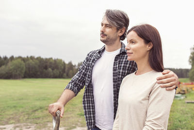 Thoughtful mid adult couple standing arm around at organic farm