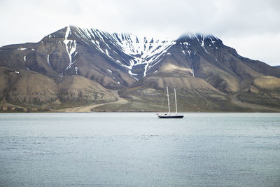 Sailboat on sea by snowcapped mountain against sky