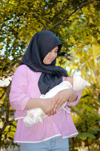 Mother carrying baby girl while standing in park