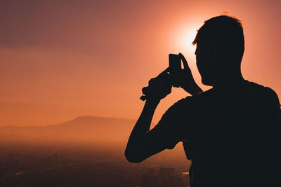 Rear view of silhouette man photographing against sky during sunset