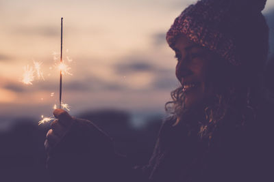 Side view of woman holding sparkler against sky