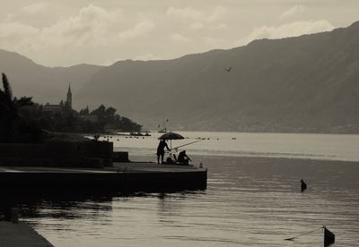 Silhouette man fishing in sea against sky