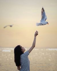 Low angle view of woman feeding bird flying over sea against sky