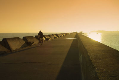Silhouette man riding bicycle on pier