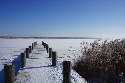 Wooden posts on snow covered land against clear blue sky