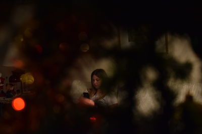 Woman using mobile phone seen through christmas tree