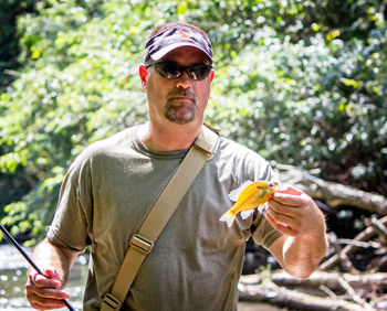 Portrait of man holding fish while fishing in lake