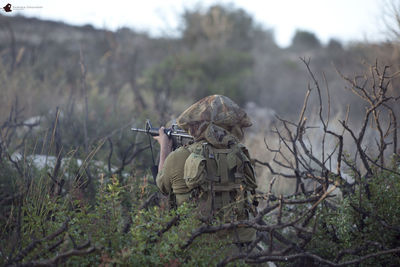 Rear view of soldier aiming with sniper on field