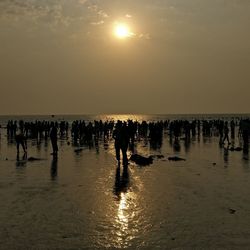 Silhouette people walking on beach against sky during sunset