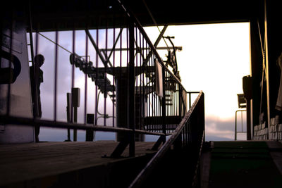 Silhouette bridge by buildings against sky during sunset