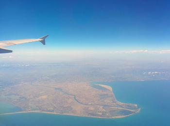 Aerial view of airplane wing over landscape against blue sky