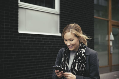 Smiling mid adult businesswoman using mobile phone on sidewalk