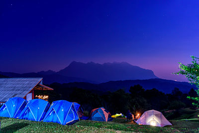 Tent on field by mountains against blue sky at night