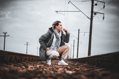 Full length of woman crouching on railroad track against sky