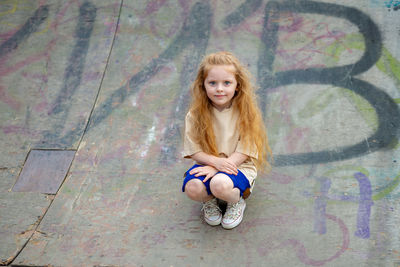 Portrait of smiling cute girl crouching on sports ramp