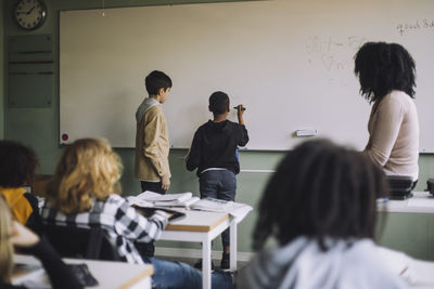 Students solving maths sum on white board in classroom