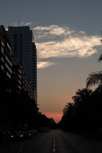 Road by buildings against sky during sunset