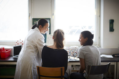 Smiling mature chemistry teacher with young students in classroom