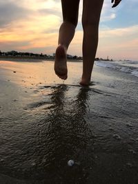 Low section of woman wading in sea during sunset