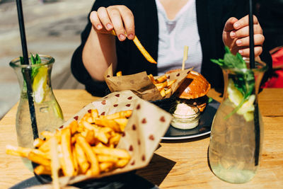 Midsection of woman having french fries while sitting at table