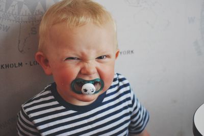 Portrait of angry baby boy sucking pacifier at home