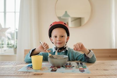 Boy sat at the dinner table smiling with his helmet on eager to cycle