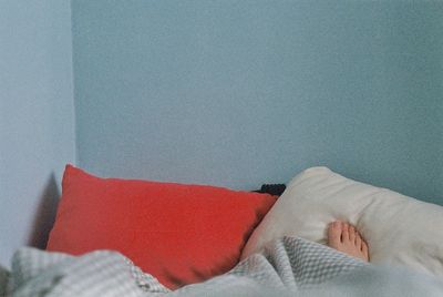 Low section of person relaxing on bed against wall