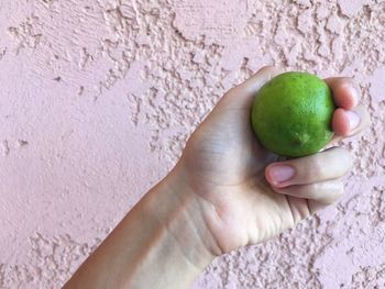 Cropped hand holding lime by wall