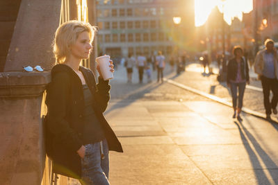 Young blond woman drinking coffe in sunset light outdoor on a city street