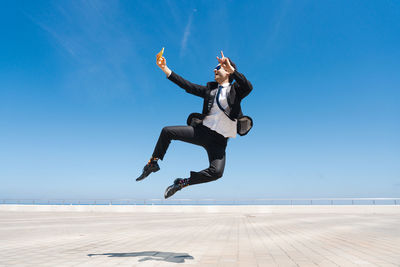 Full length of woman jumping at beach against clear blue sky