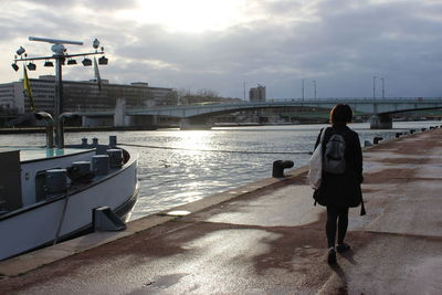 Rear view of woman standing on railing by river against sky