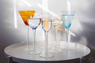 Group of tall long-stemmed cocktail glasses in different shapes and colours filled with clear liquid