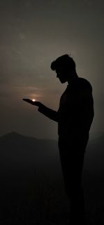 Side view of silhouette man standing on field against sky during sunset